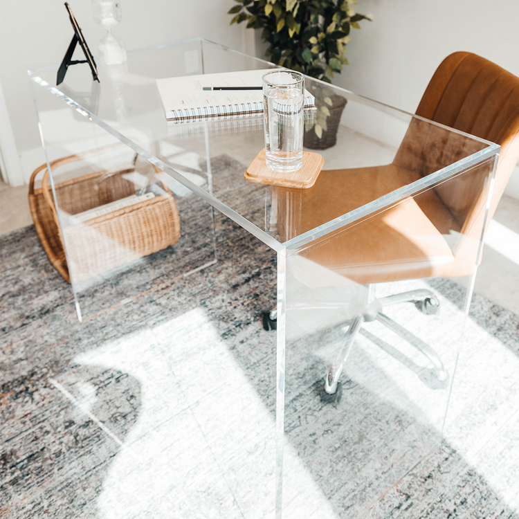 An acrylic lucite slab desk with a brown leather chair in front, placed in an office setting.