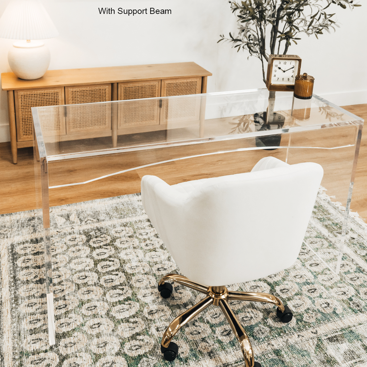 An acrylic lucite slab desk with a white chair in front, placed in an office setting with a painting on the wall and a tree in the background.