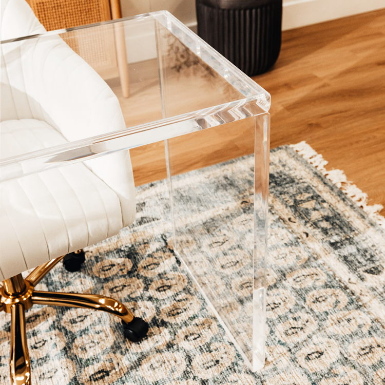 A closeup of the corners on an acrylic lucite slab desk with a white chair in front.