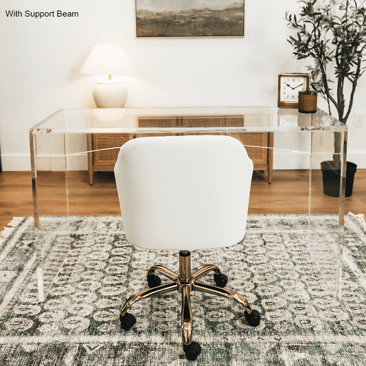 An acrylic lucite slab desk with a white chair in front, placed in an office setting with a painting on the wall and a tree in the background.