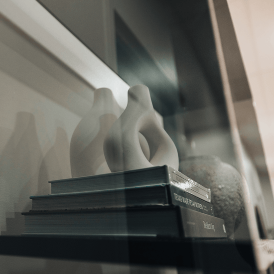 Closeup of a vertical smoke gray acrylic 4 interior shelf bookcase decorated with vases, books, and decor placed against a white wall in a living room.