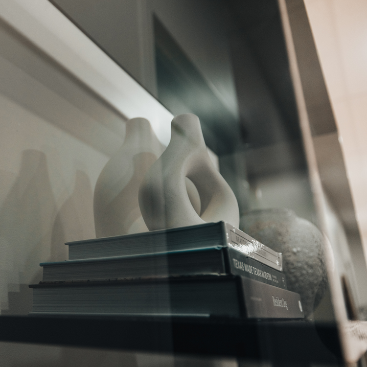 Closeup of a vertical smoke gray acrylic 4 interior shelf bookcase decorated with vases, books, and decor placed against a white wall in a living room.