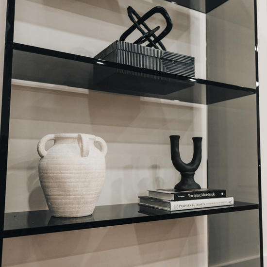 Closeup of a vertical smoke gray acrylic 4 interior shelf bookcase decorated with vases, books, and decor placed against a white wall in a living room.