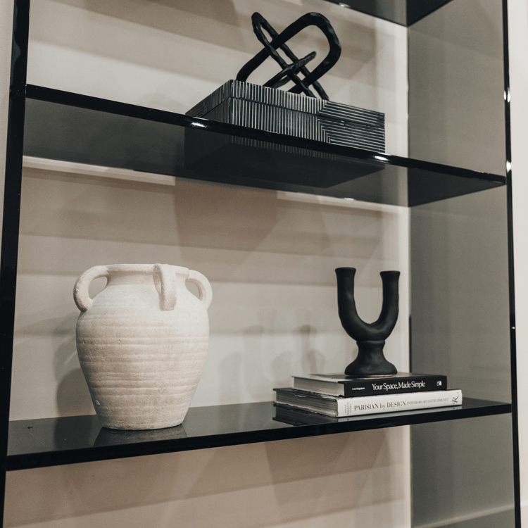 Closeup of a vertical smoke gray acrylic 4 interior shelf bookcase decorated with vases, books, and decor placed against a white wall in a living room.