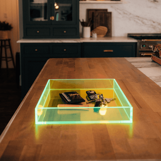 A clear neon glowing green tinted square acrylic tray w/ sides placed on a kitchen counter holding keys and a wallet.
