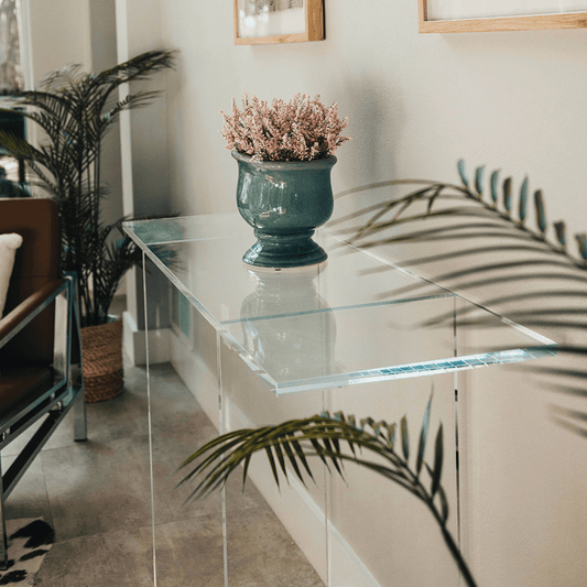 Clear acrylic lucite console table with a decorative vase and plant in a living room setting.