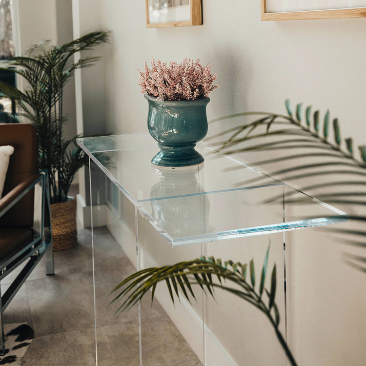 Clear acrylic lucite console table with a decorative vase and plant in a living room setting.