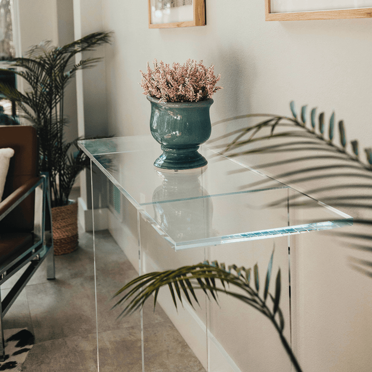 Clear acrylic lucite console table with a decorative vase and plant in a living room setting.