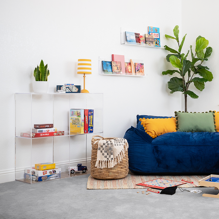 Clear acrylic 4 cube storage unit displaying a plant, lamp, books, and games in a child's playroom. Also featured is a set of 2 floating bookshelves mounted on the wall displaying books. The unit features 2 rows of 2 cubes.