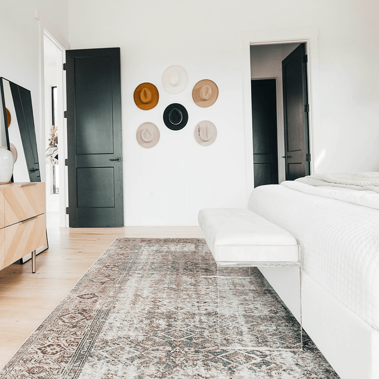 An elegant clear acrylic lucite white velvet leather upholstered bench at the foot of a bed in a stylishly decorated bedroom setting.