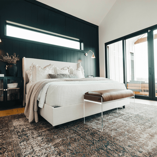 An elegant clear acrylic lucite brown leather upholstered bench at the foot of a bed in a stylishly decorated bedroom setting.