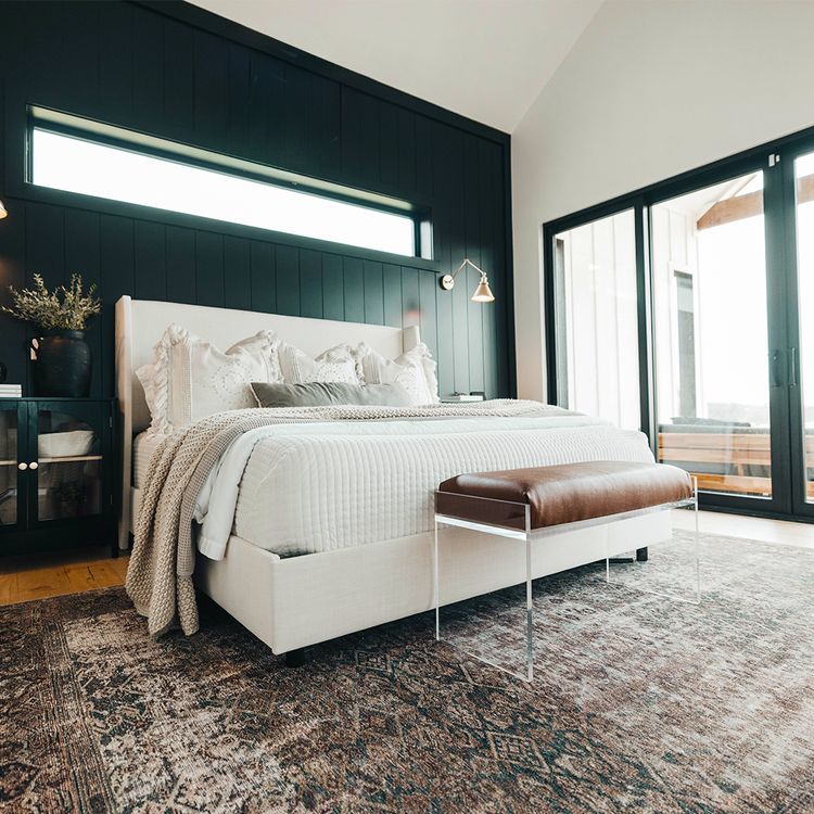 An elegant acrylic lucite brown leather upholstered bench at the foot of a bed in a stylishly decorated bedroom setting.