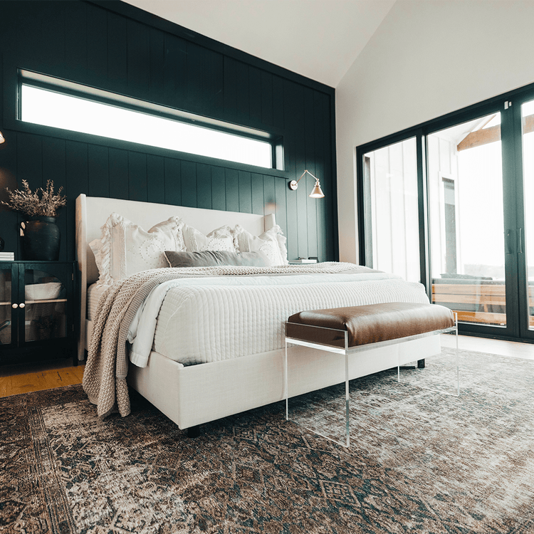 An elegant clear acrylic lucite brown leather upholstered bench at the foot of a bed in a stylishly decorated bedroom setting.