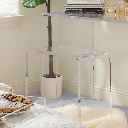 Closeup of a clear acrylic vanity stool next to its partnering vanity table in a bedroom.