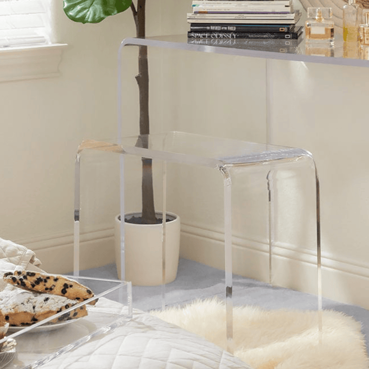 Closeup of a clear acrylic vanity stool next to its partnering vanity table in a bedroom.