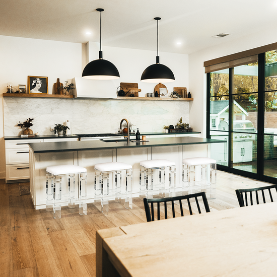 4 clear acrylic lucite barstools with white padded seats placed at a kitchen island.