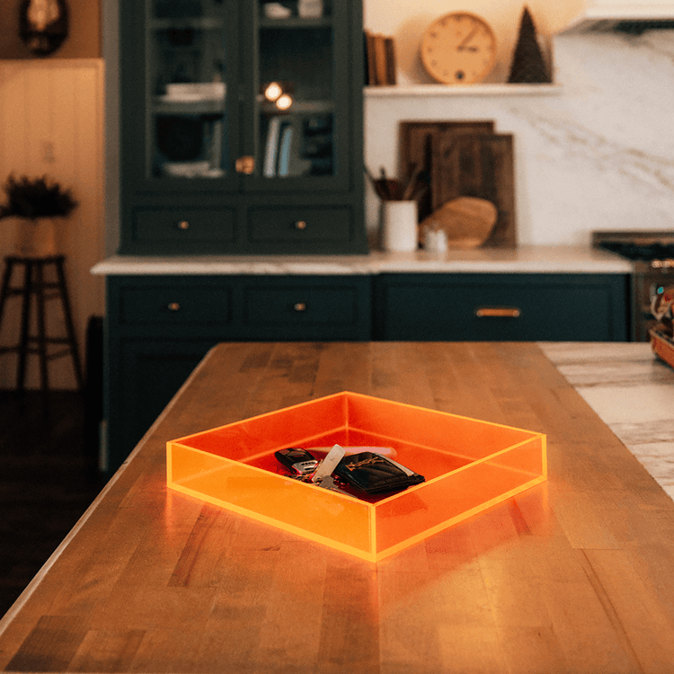 Square shaped neon orange tray on a wooden table in a kitchen setting.