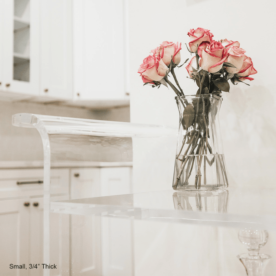 A closeup of the handle and top shelf of a clear acrylic bar cart decorated with a clear vase of roses.