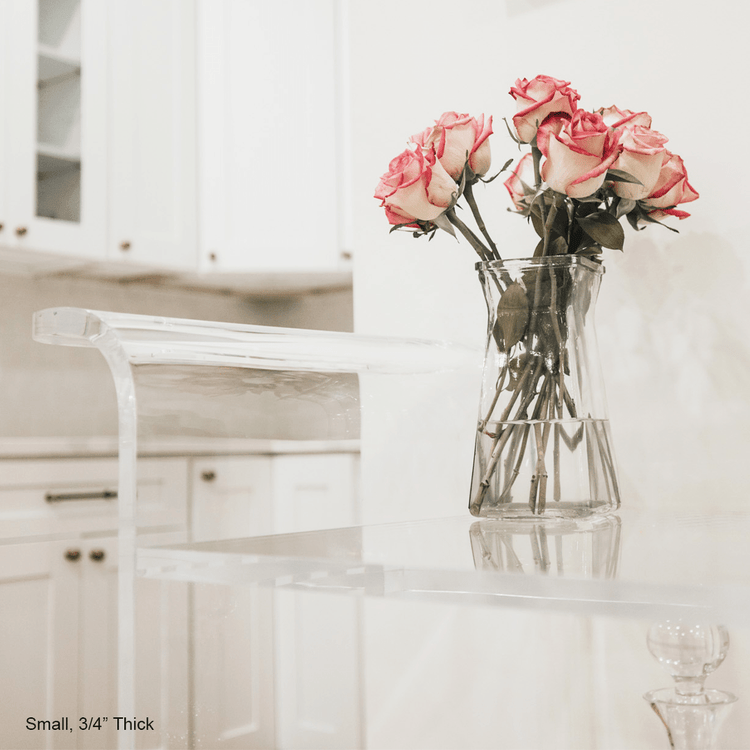 A closeup of the handle and top shelf of a clear acrylic bar cart decorated with a clear vase of roses.
