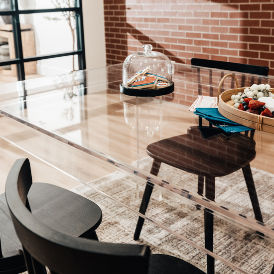 A clear acrylic lucite dining table decorated with snacks surrounded with black chairs.