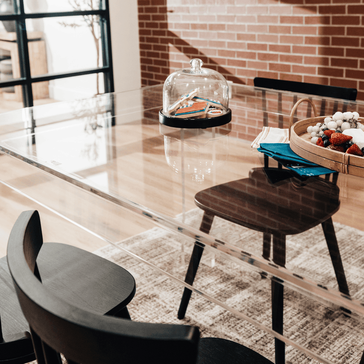 A clear acrylic lucite dining table decorated with snacks surrounded with black chairs.