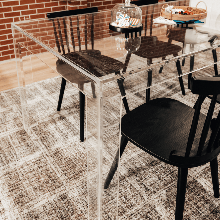 A clear acrylic lucite dining table decorated with snacks surrounded with black chairs.