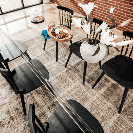A clear acrylic lucite dining table decorated with snacks and a vase of flowers surrounded with black chairs.