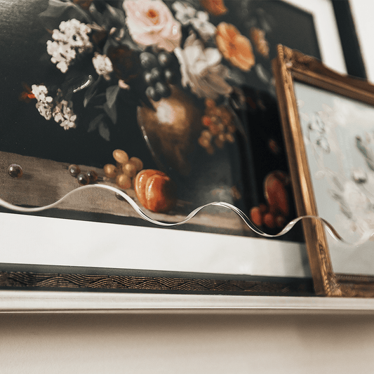 A closeup of the wavy edge on a clear acrylic floating bookshelf holding famed floral artwork.