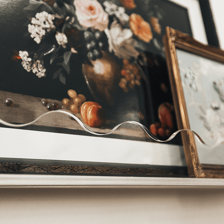 A closeup of the wavy edge on a clear acrylic floating bookshelf holding famed floral artwork.