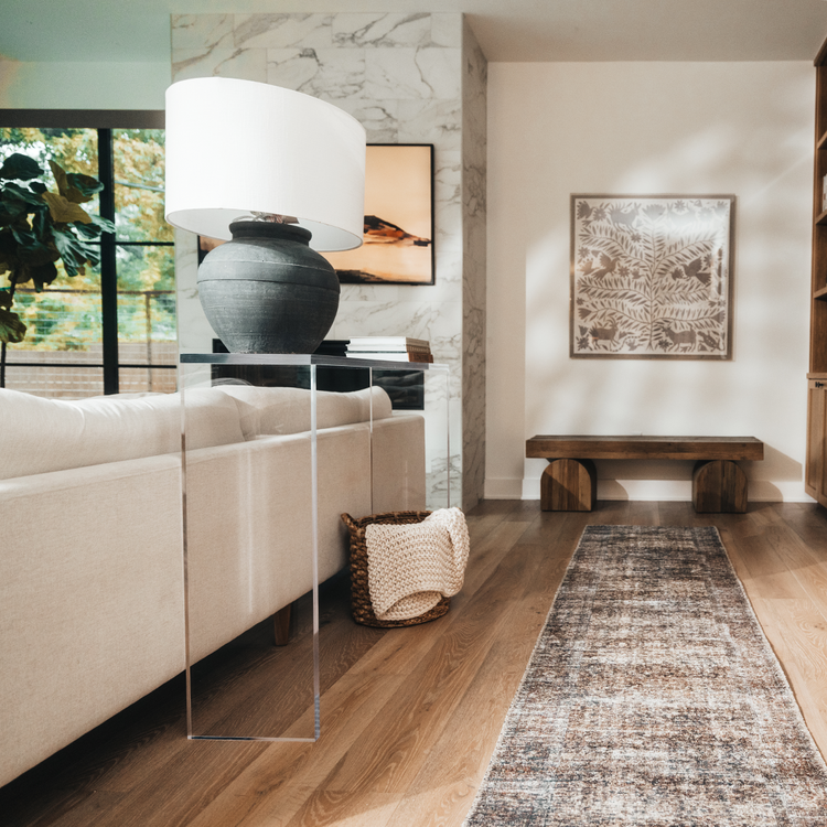A modern clear acrylic console table with a slab style reflective surface, placed in a room with a beige sofa and decorative items on top.