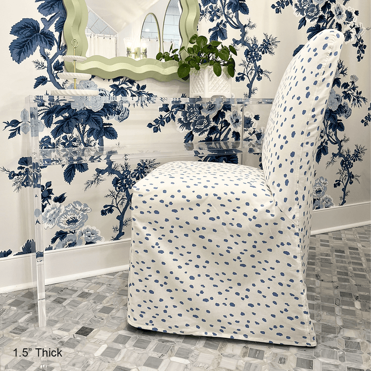 A clear acrylic console table with 1 interior shelf decorated with a jewelry dish and a plant placed against a wall with floral wallpaper and a mirror. An upholstered chair is partial underneath.