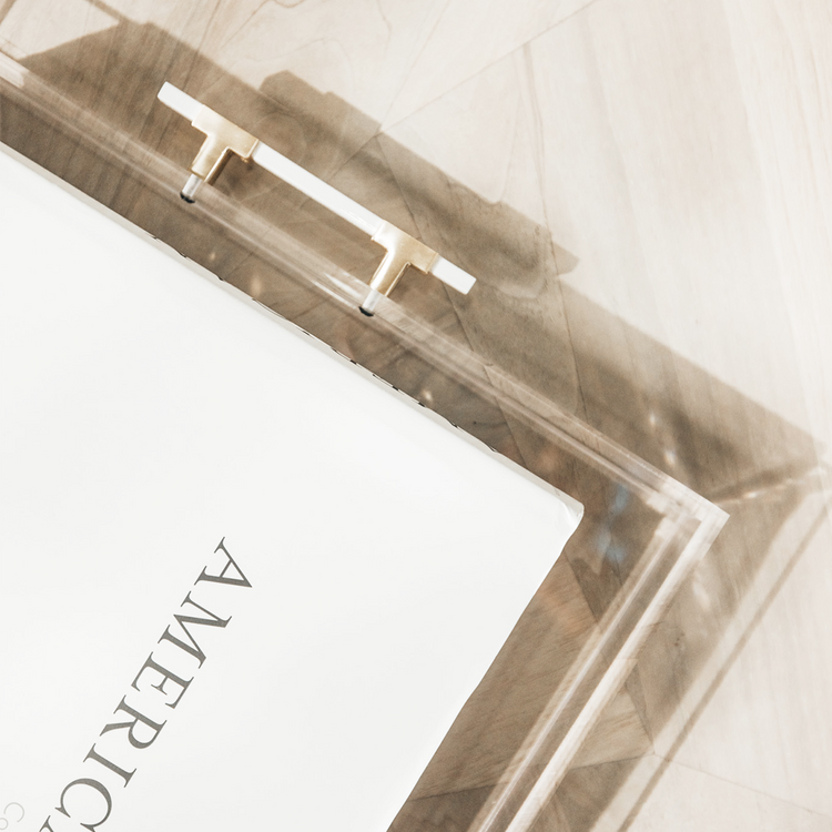 A closeup of the white and gold handle on a clear acrylic lucite serving tray displaying a book.