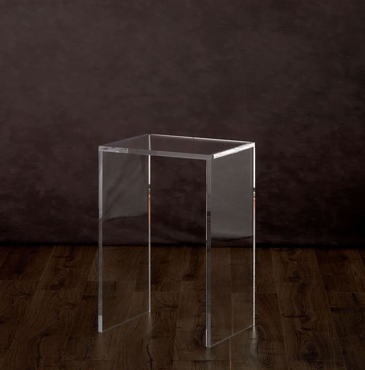 A catalog view of a vertical rectangular shaped acrylic side table placed on a hardwood floor.