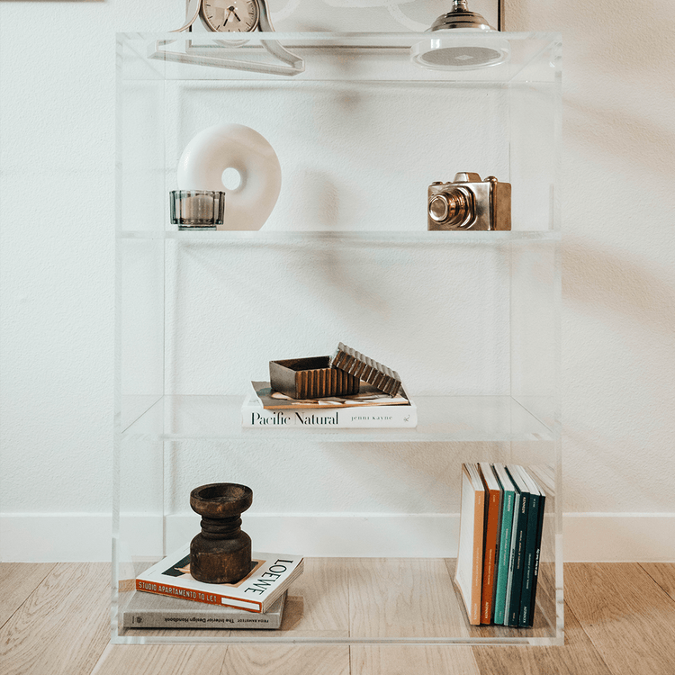 Clear acrylic lucite bookshelf with 3 interior shelves displaying books and decor.