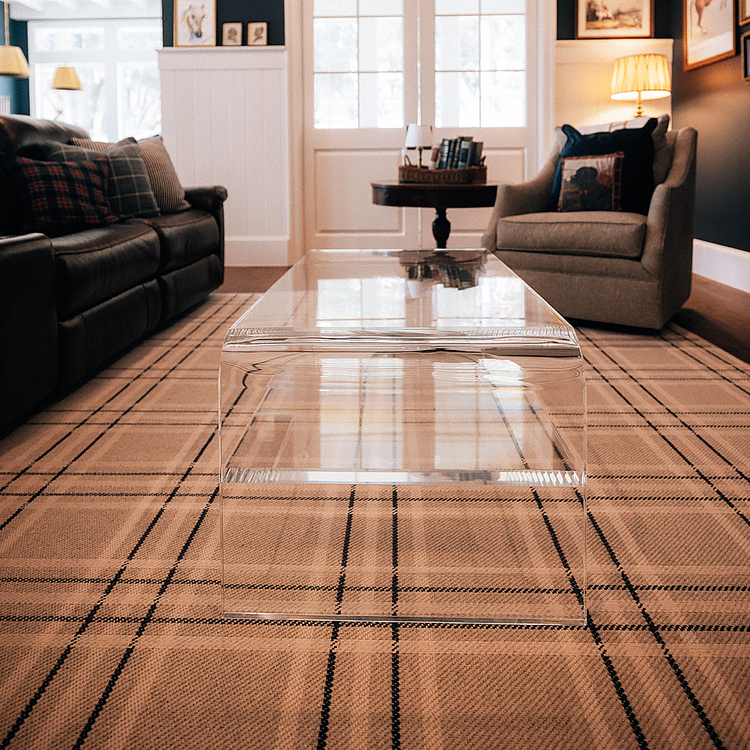 Living room with a leather couch, upholstered armchair, and a clear acrylic waterfall edge coffee table placed on a plaid rug. 