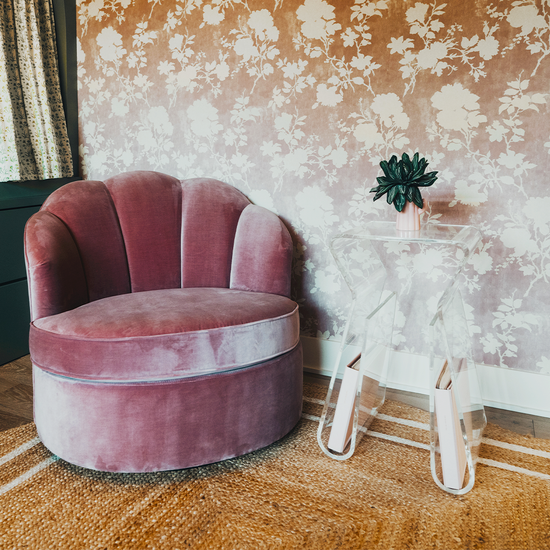 An acrylic lucite side table featuring legs that curve up into the inside of the table to double as a book or magazine rack sitting beside an easy chair. 