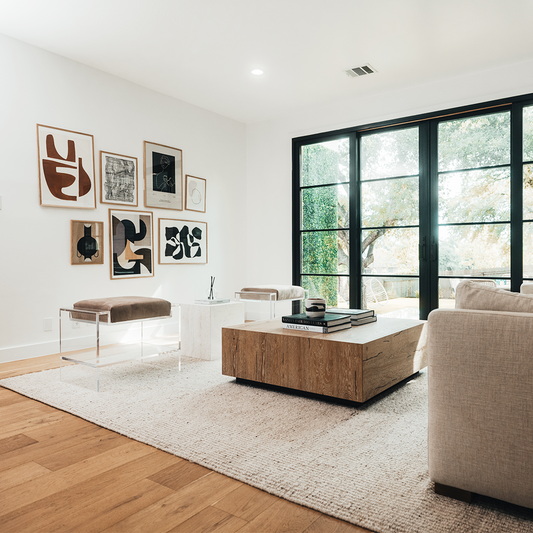 Two clear acrylic benches with brown cushions and storage shelf underneath, placed as extra seating in a modern living room with abstract art on the walls.