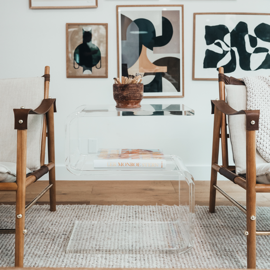 A clear acrylic side table shaped like the number 5 placed between 2 chairs in a living room.