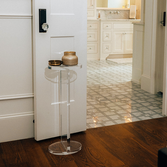 Clear acrylic side table with decorative items in a bathroom setting next to a door.