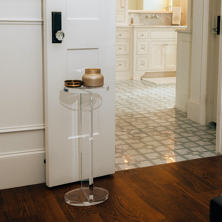 Clear acrylic side table with decorative items in a bathroom setting next to a door.