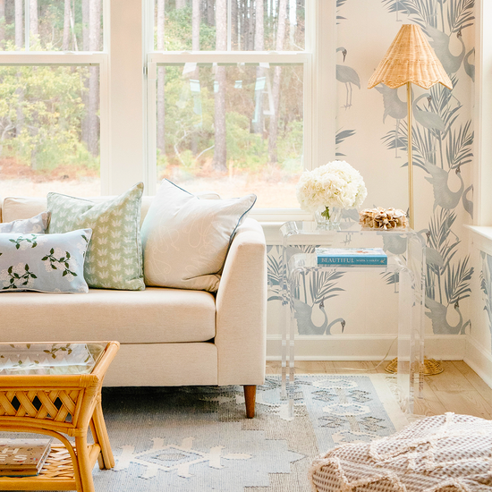 A clear acrylic nesting end table set placed in a living room setting beside a white sofa, with a lamp and decorative items on top.