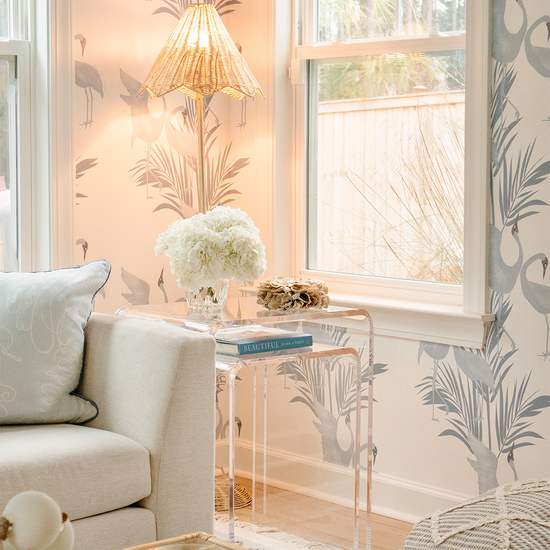 A clear acrylic nesting end table set placed in a living room setting beside a white sofa, with a lamp and decorative items on top.