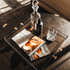A clear acrylic lucite serving tray with gold and black handles holding a glass liquor carafe, glasses and drink receipe books placed on top of a coffee table.