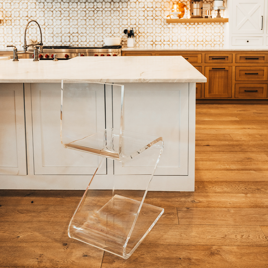 A clear acrylic bar stool with a modern design, placed in a kitchen setting next to a white countertop.