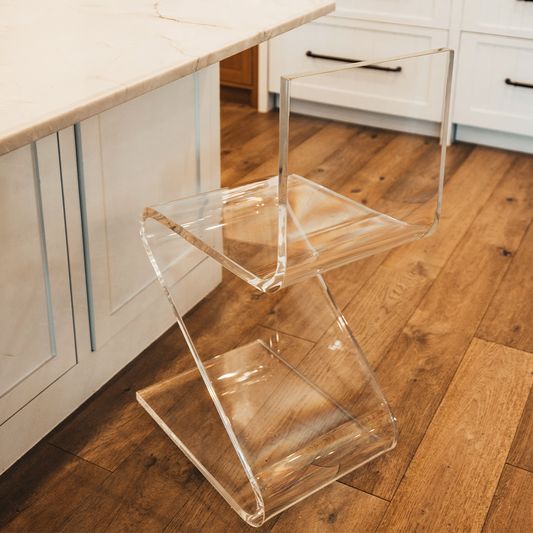 A clear acrylic bar stool with a modern design, placed in a kitchen setting next to a white countertop.
