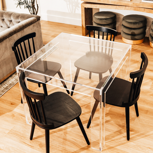  A square clear acrylic lucite game table featuring a chair on each side in a living room.  