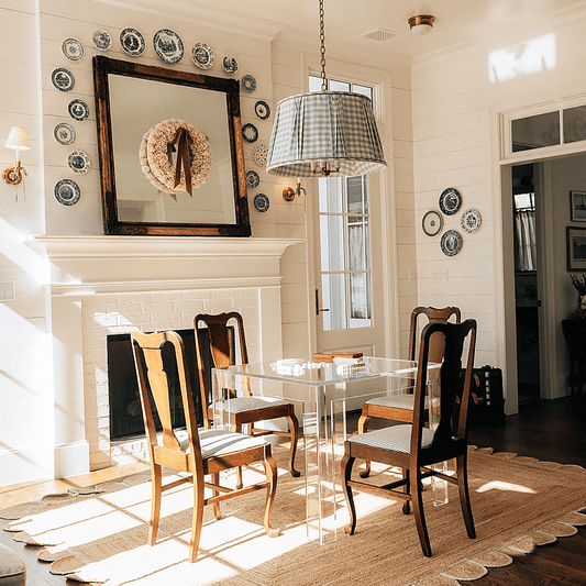 A square clear acrylic lucite game table set up for tile game playing with seating for 1 on each side in a brightly lit living room next to a fireplace.