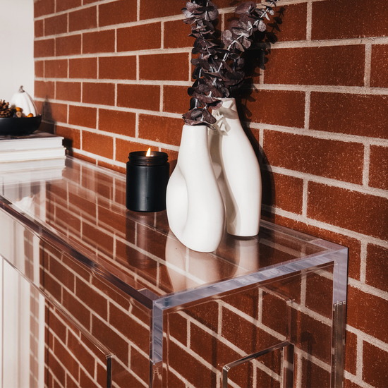Clear acrylic slab entryway table in front of a brick wall displaying books, a candle, and decor.