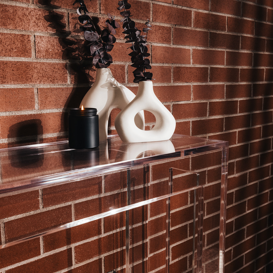 Clear acrylic slab entryway table in front of a brick wall displaying a candle and decor.
