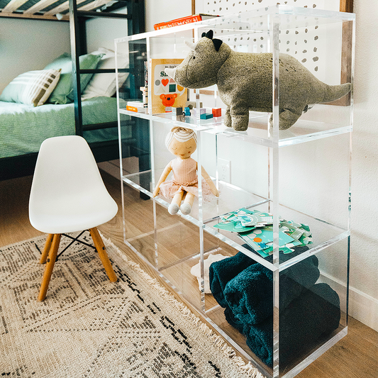 A clear acrylic lucite 9 cube storage unit displaying children's toys, blankets, and books in a child's bedroom. The unit features 3 rows of 3 cubes.